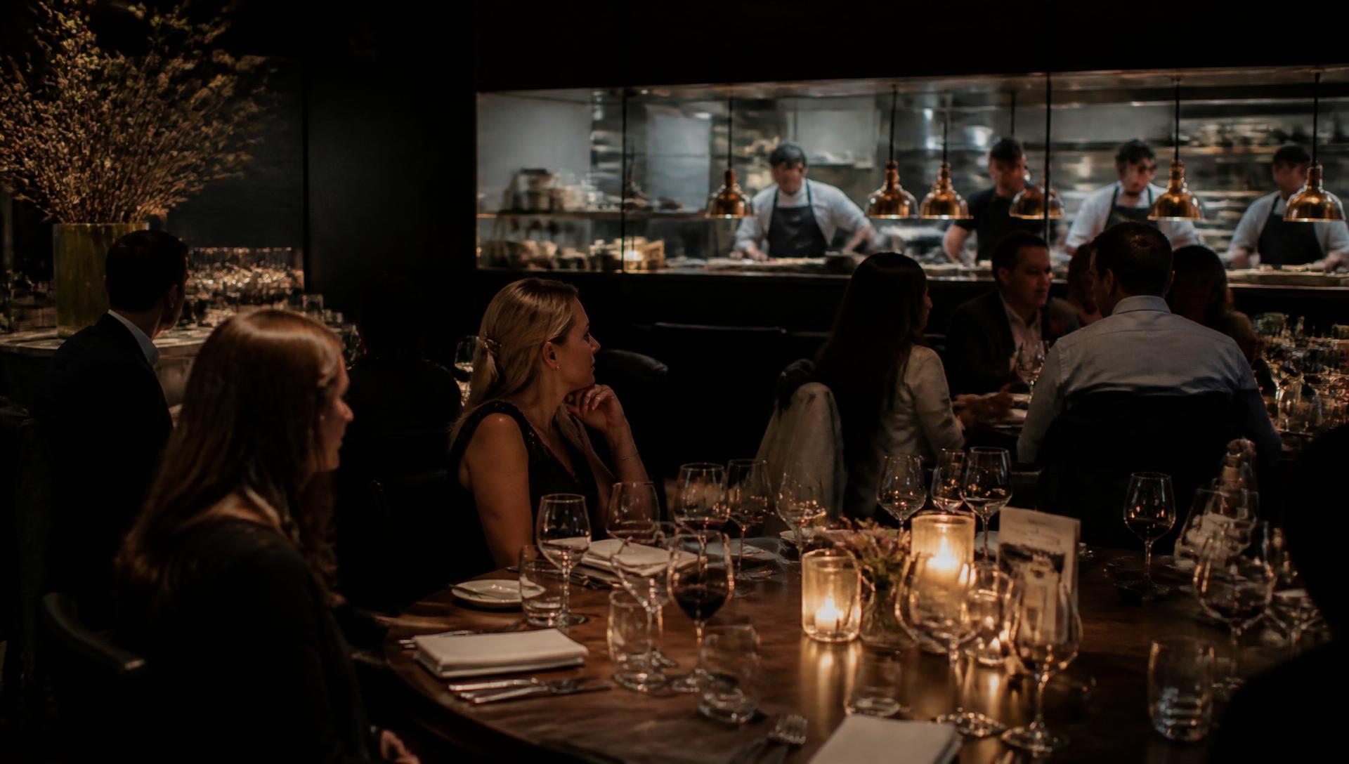 Candlelit fine dining room with an open kitchen and chefs at the pass